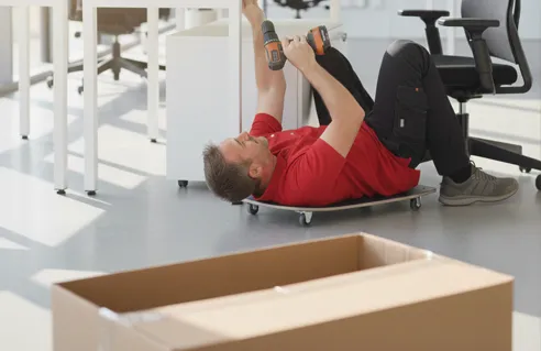 Monteur beim Aufbau einer Büroeinrichtung, Paket im Vordergrund